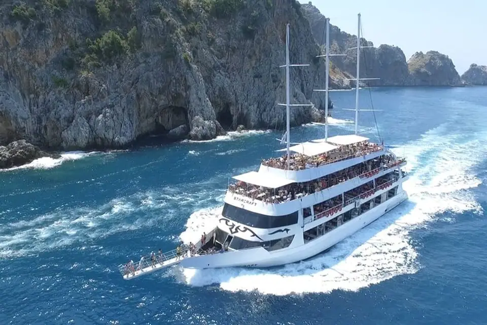 A large white multi-deck tour boat cruising past rocky cliffs on deep blue water