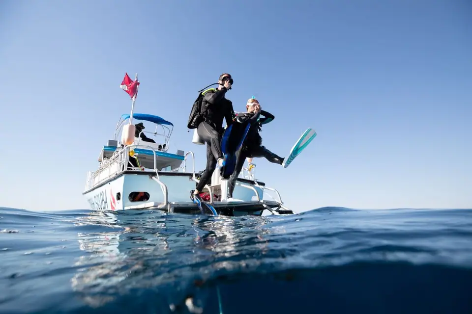 Two divers in full gear stepping off a dive boat into clear blue water