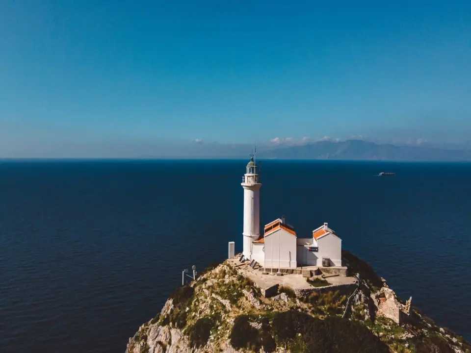 The white Deveboynu lighthouse and its red-roofed keeper's house on a rocky cape above a deep blue sea