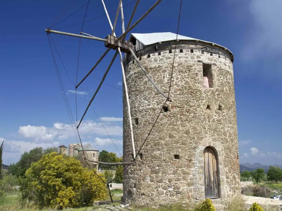 An old round stone windmill with wooden sails under a blue sky